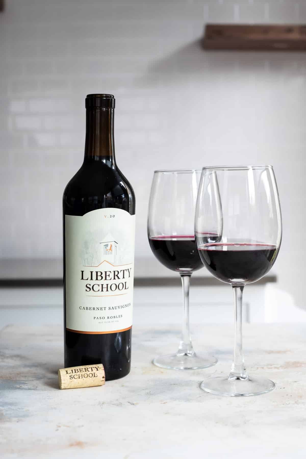 A bottle of red wine next to 2 glasses of the same.