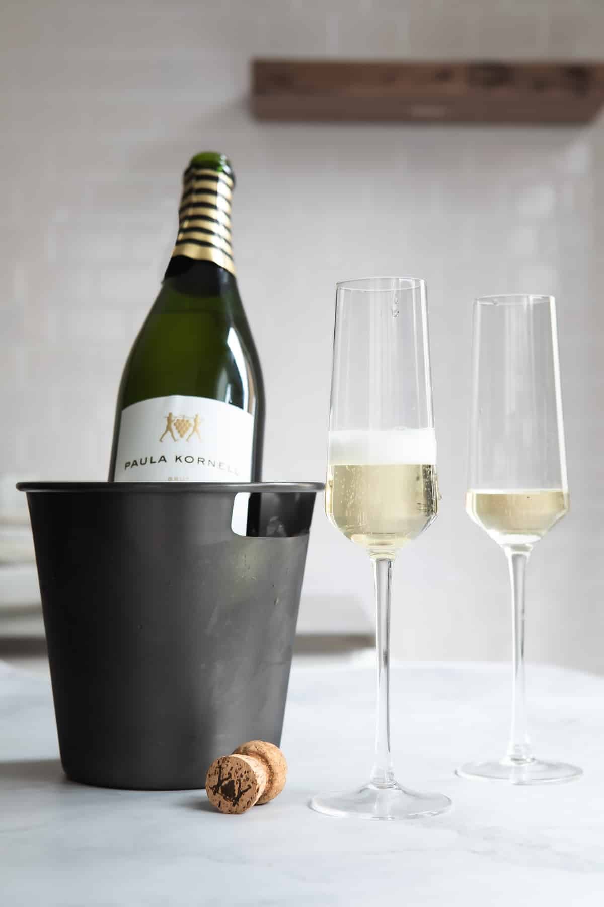 A bottle of champagne chilling near 2 full glasses.