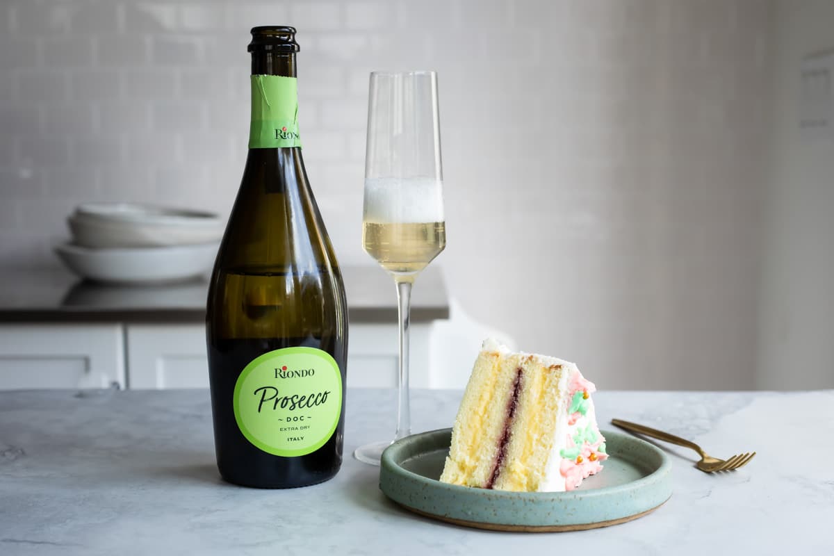 A bottle and flute of champagne next to a plate of Danish layer cake.