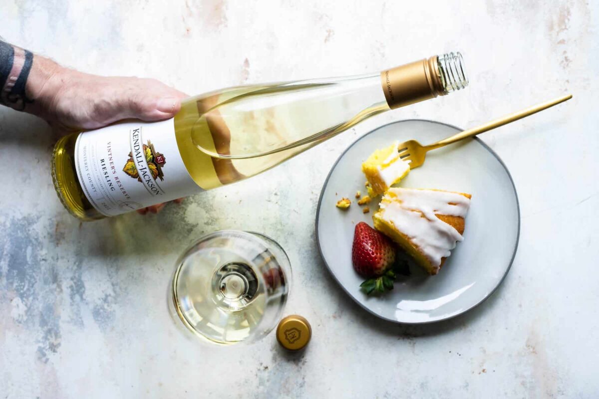 A bottle and glass of white wine next to a slice of lemon bundt cake.