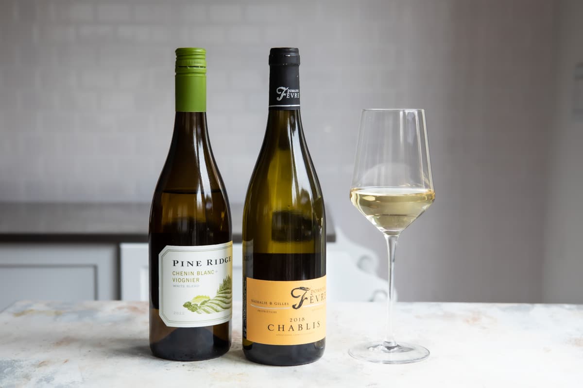 2 bottles of white wine next to a glass of the same.