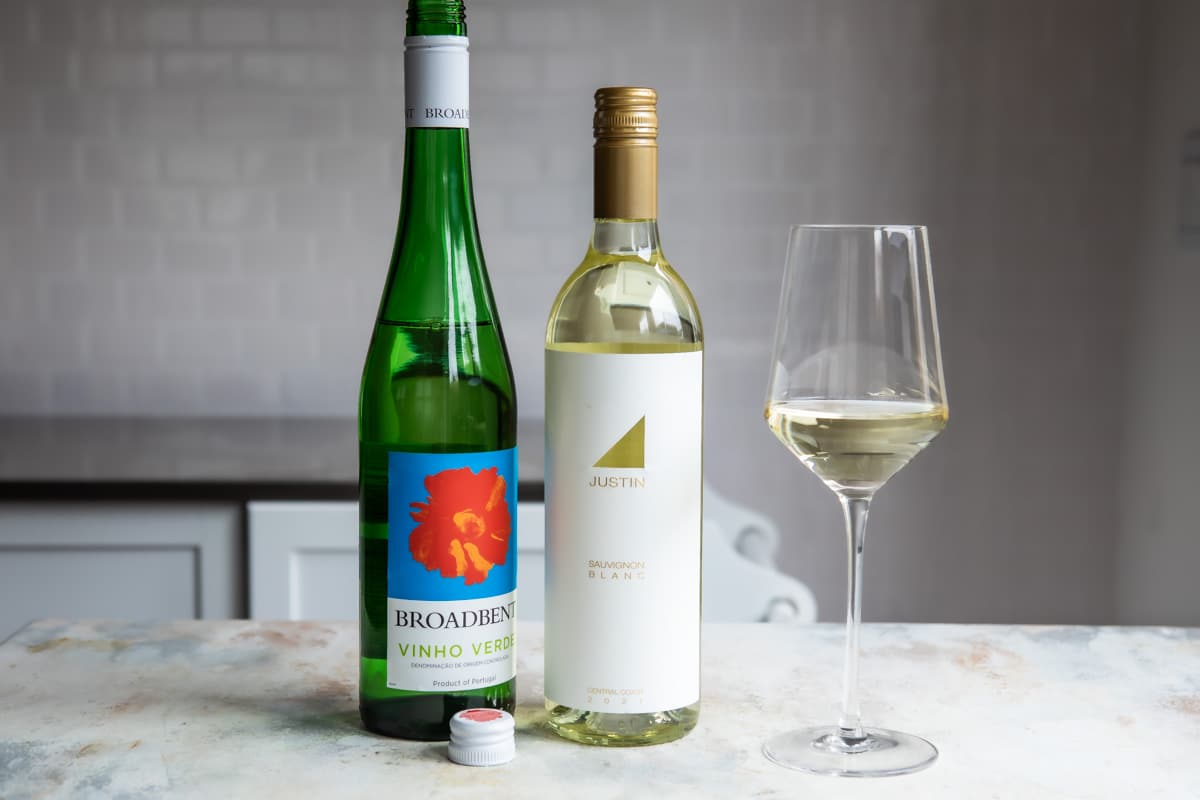 2 bottles of white wine next to a glass of the same.