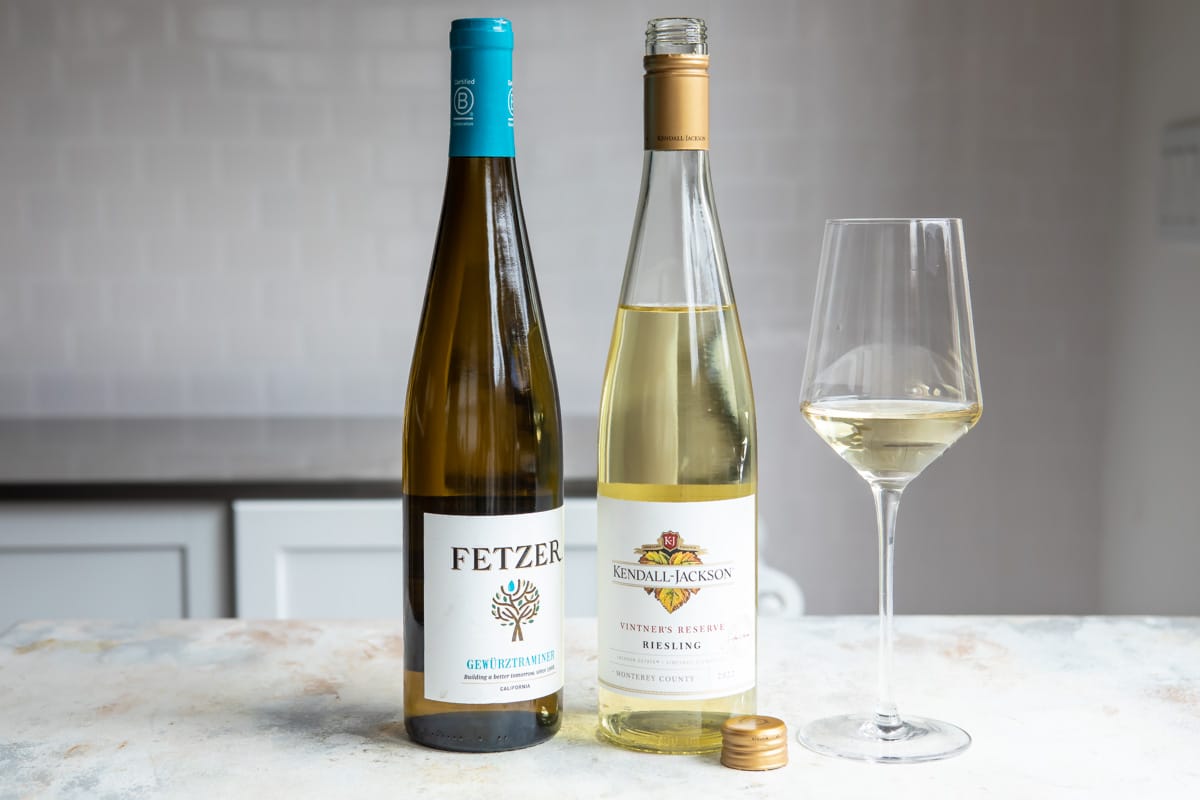 2 bottles of white wine next to a glass of the same.