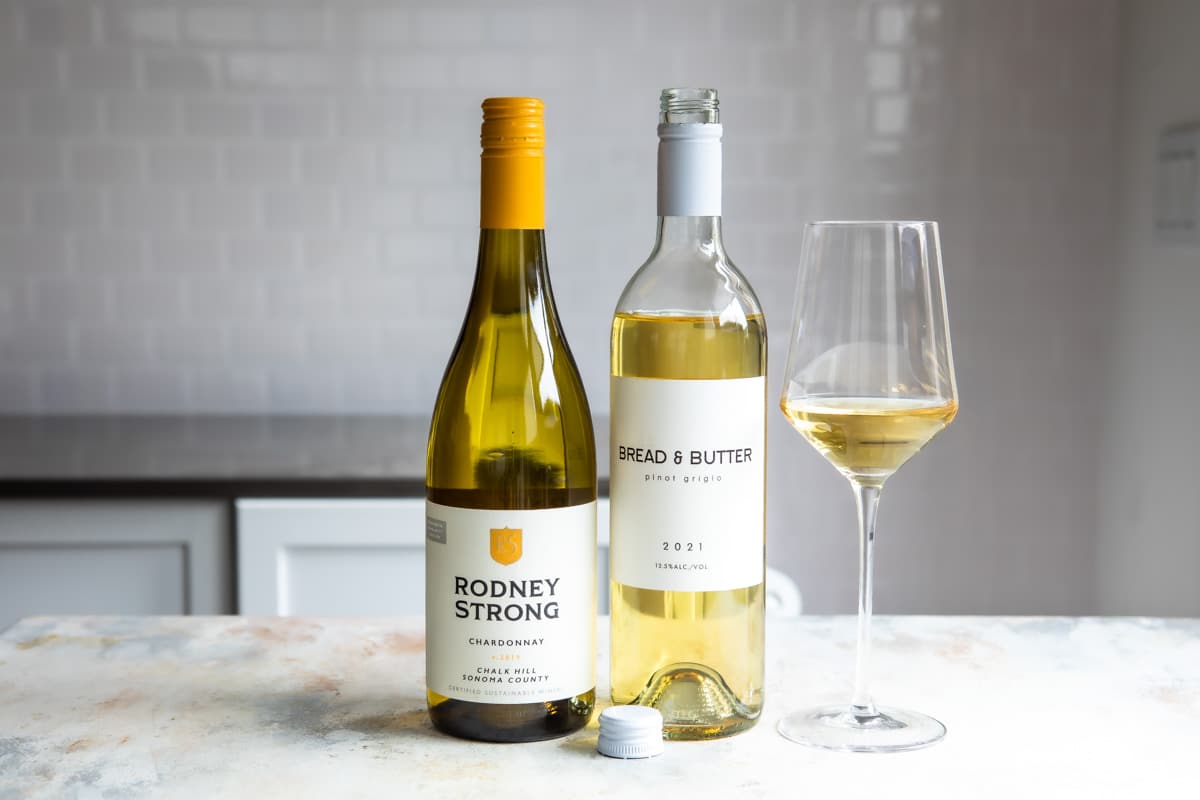 2 bottles of white wine next to a glass of the same.