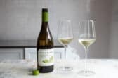 A bottle of white wine next to two glasses of the same.