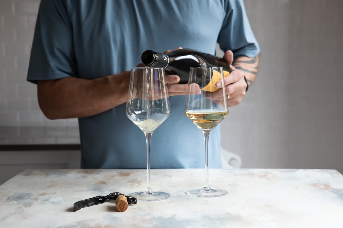 Someone pouring a glass of white wine from a bottle.