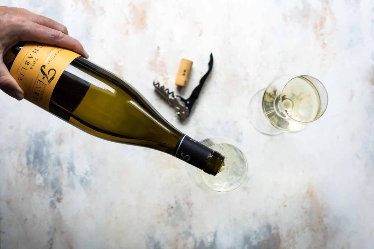 Someone pouring a glass of white wine from a bottle.