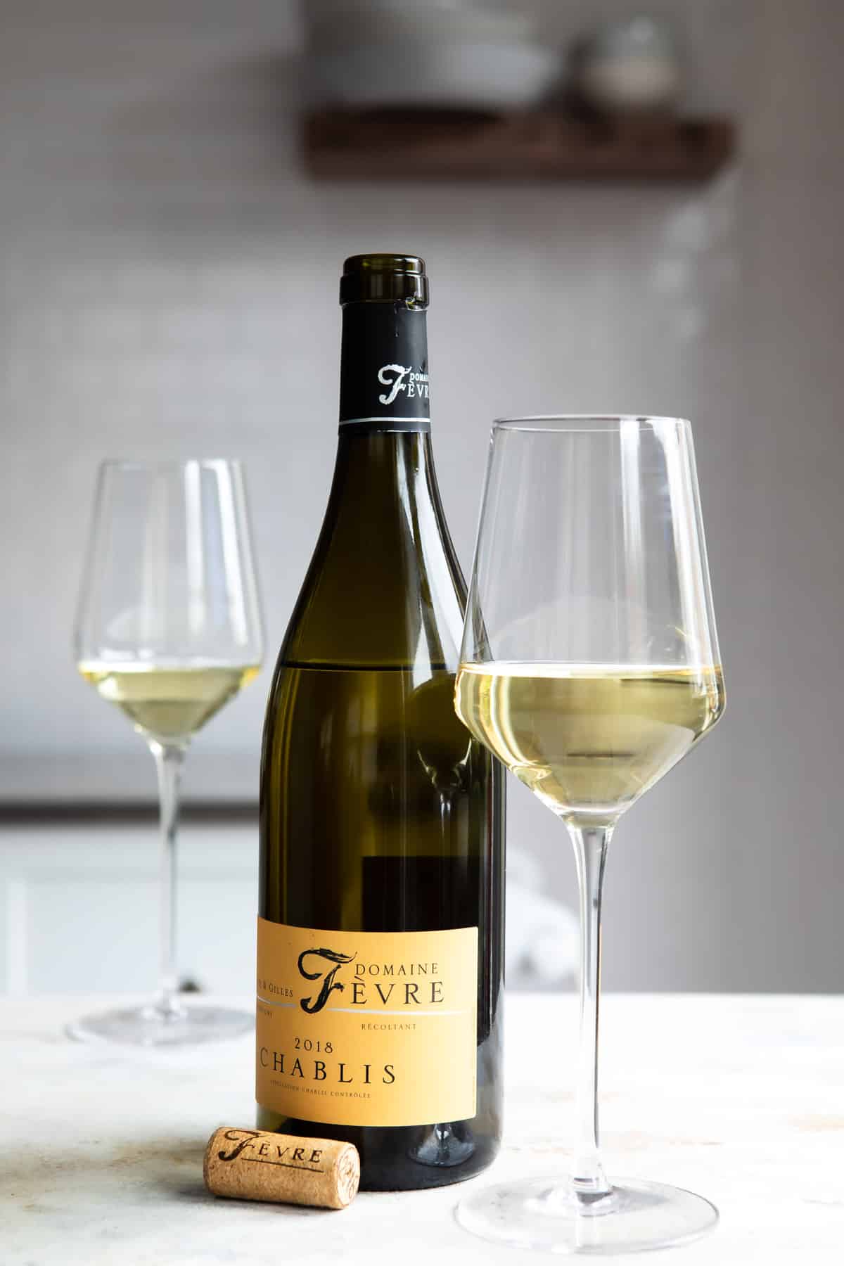 A bottle of white wine next to two glasses of the same.