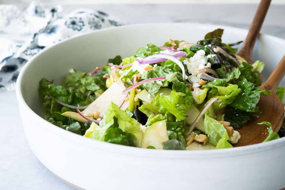 Apple walnut salad in a white serving bowl with wooden serving utensils.