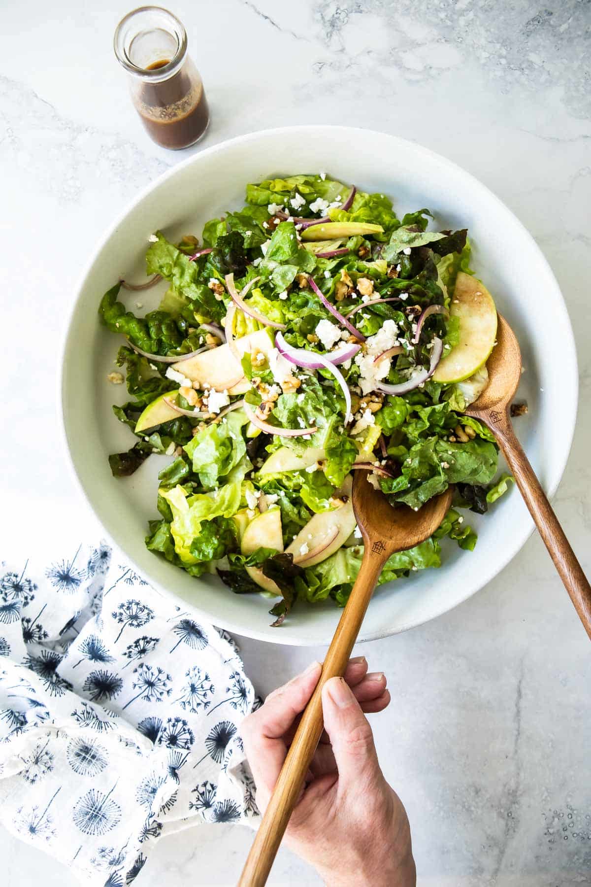 Apple walnut salad in a white serving bowl with wooden serving utensils.