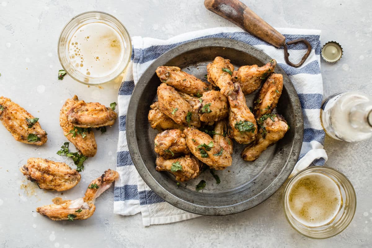 A bowl of Chinese chicken wings next to some pints of beer.