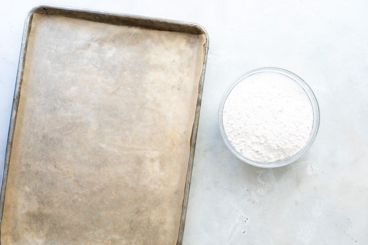 A parchment paper lined baking sheet next to a bowl of dry ingredients.