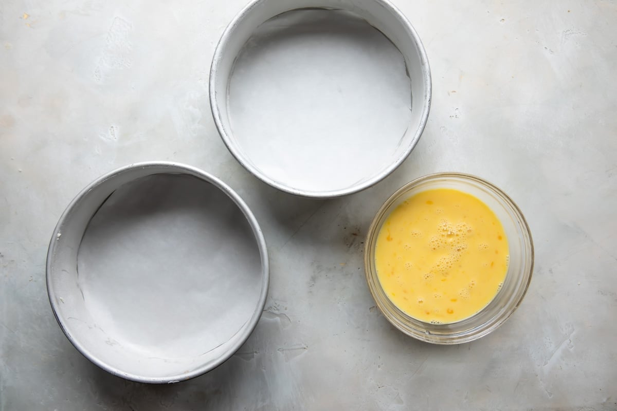 2 cake pans next to a bowl of milk, eggs, and vanilla.