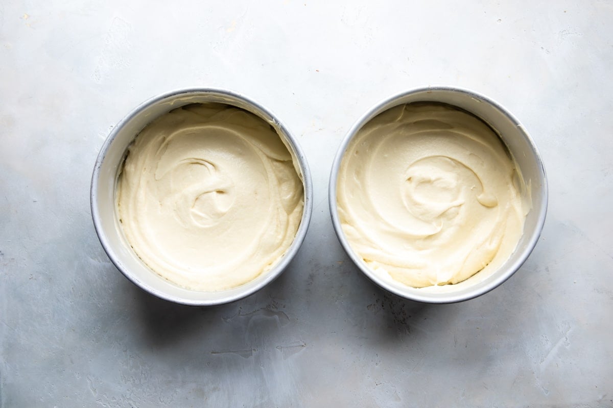 Two cake pans with vanilla cake batter in both.