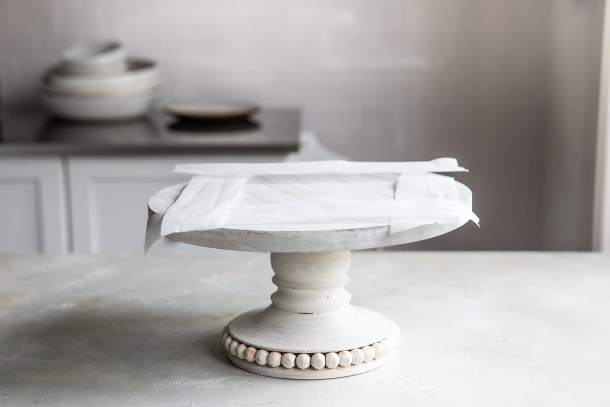 Prepping a cake stand with parchment before decorating a cake.