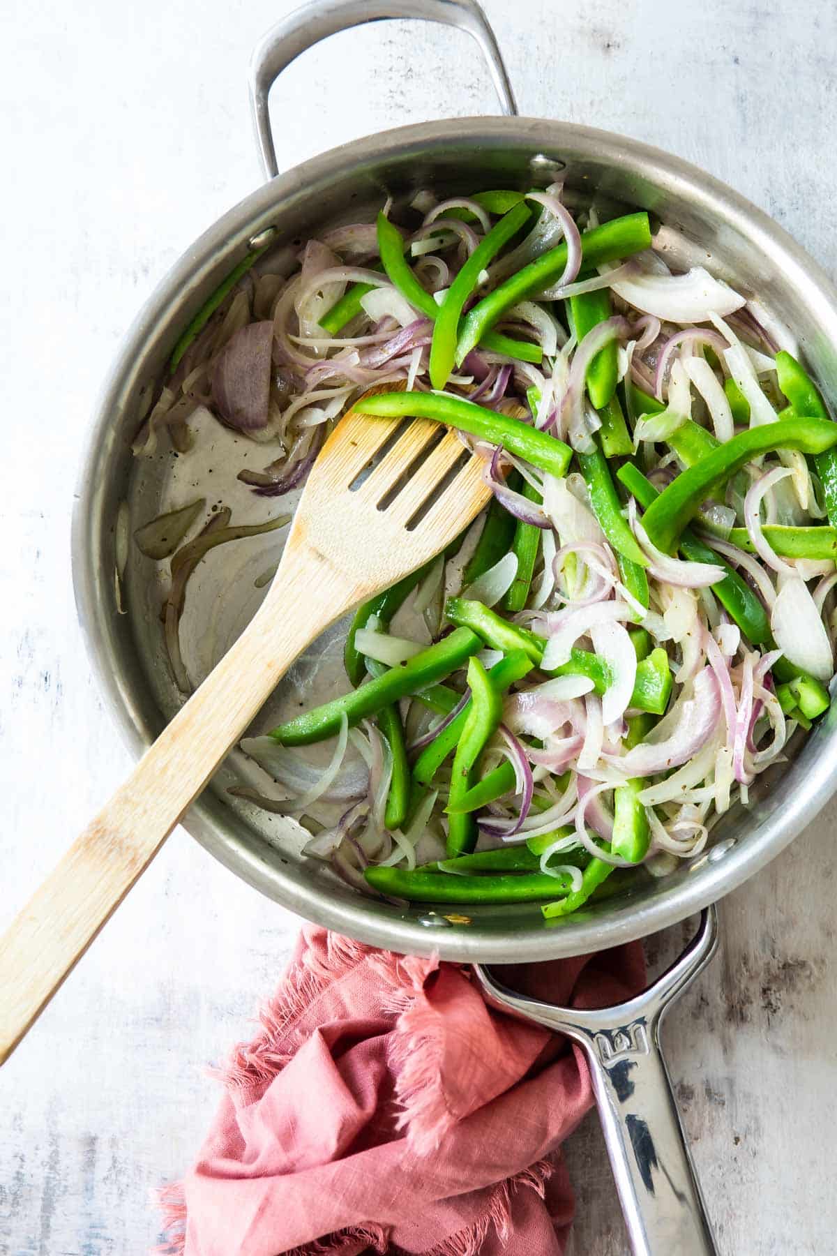 A skillet full of sliced green bell peppers and red onions for fajitas.