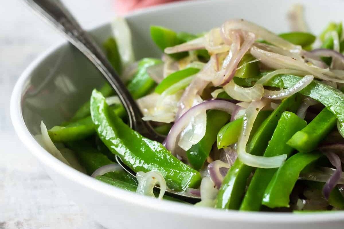 A bowl full of sliced green bell peppers and red onions for fajitas.