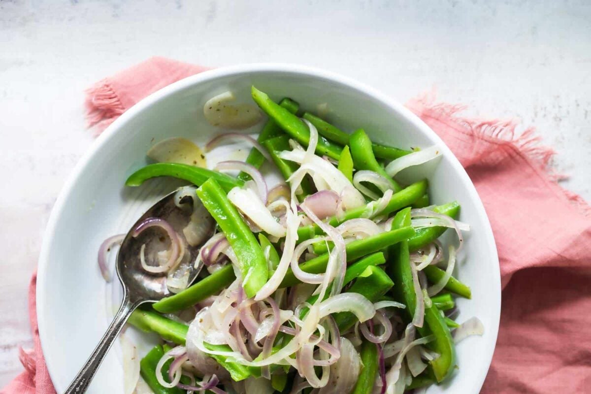 A bowl full of sliced green bell peppers and red onions for fajitas.