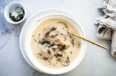 Homemade cream of mushroom soup in a white bowl with a gold spoon.