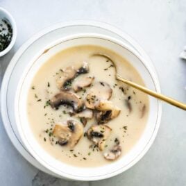 Homemade cream of mushroom soup in a white bowl with a gold spoon.