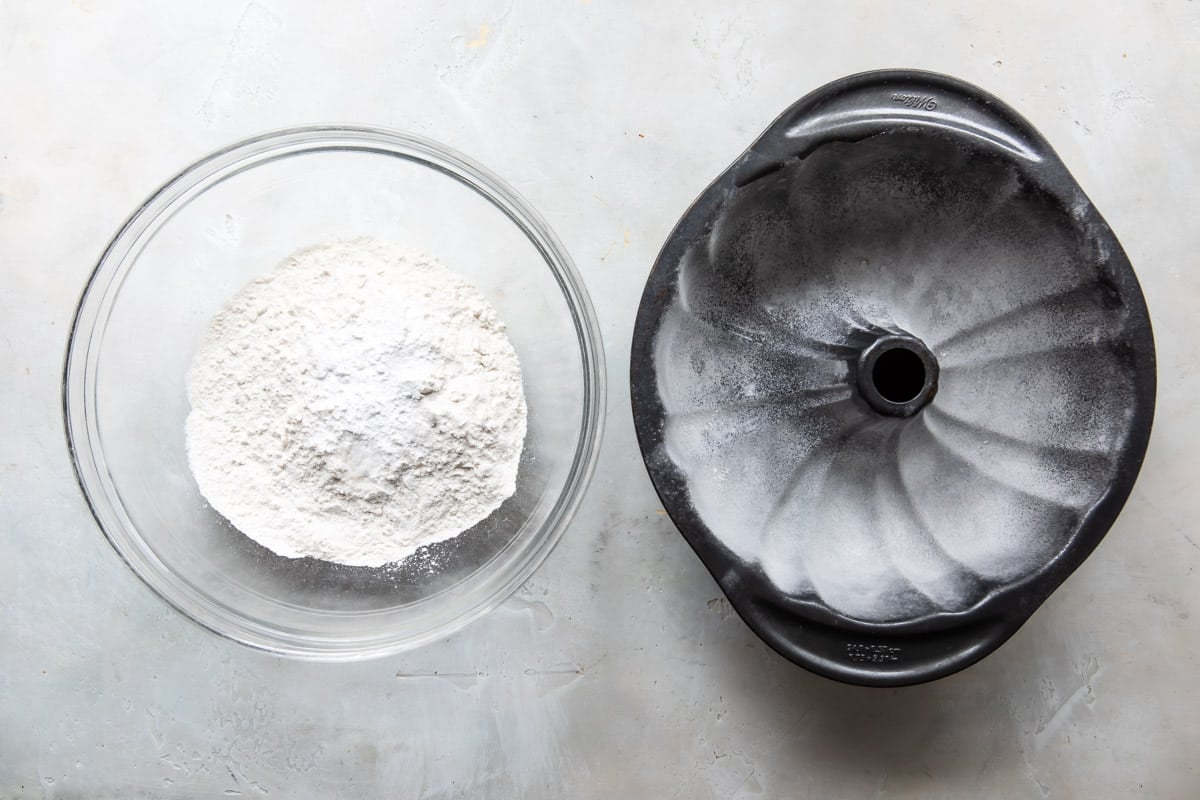 Dry ingredients for hot milk cake next to a greased bundt pan.