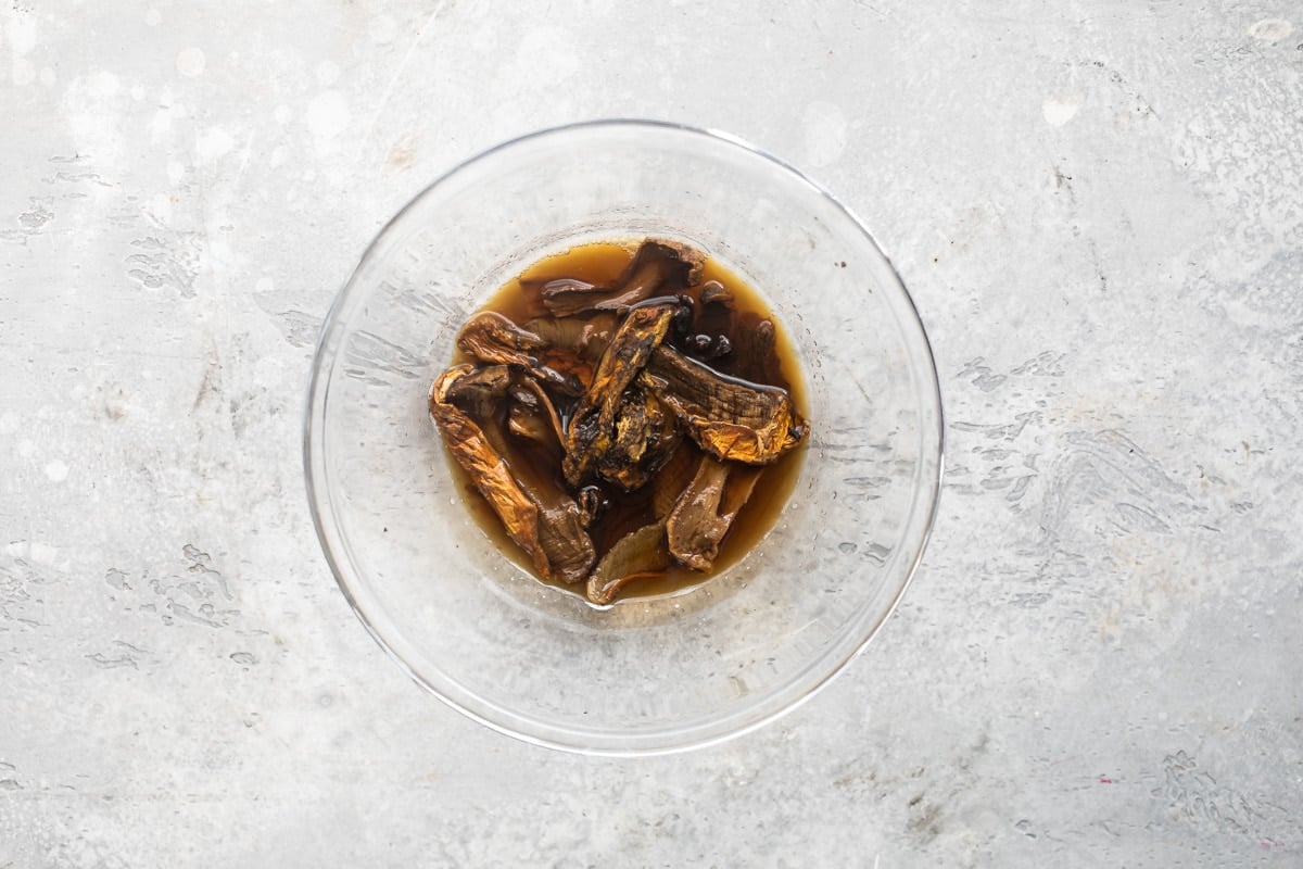 Dried porcini mushrooms soaking in a bowl of hot water to hydrate.