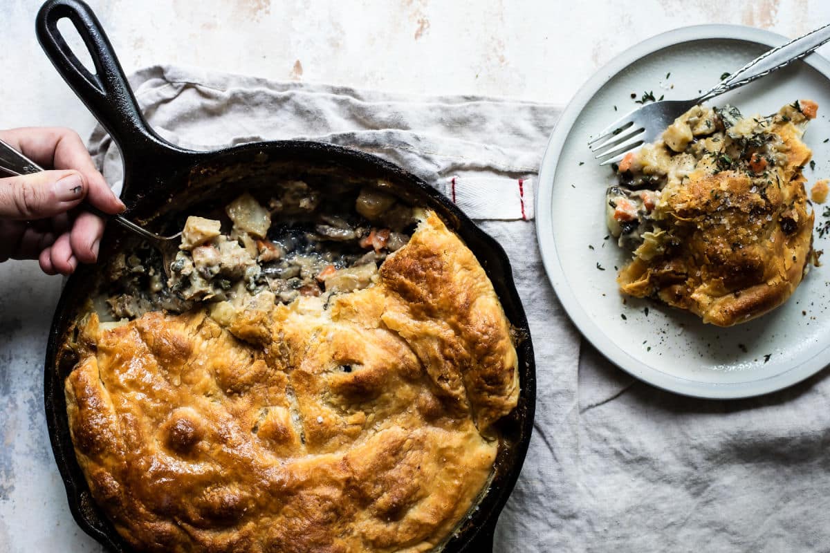 A vegetable pot pie in a cast iron skillet with some removed to a white plate.