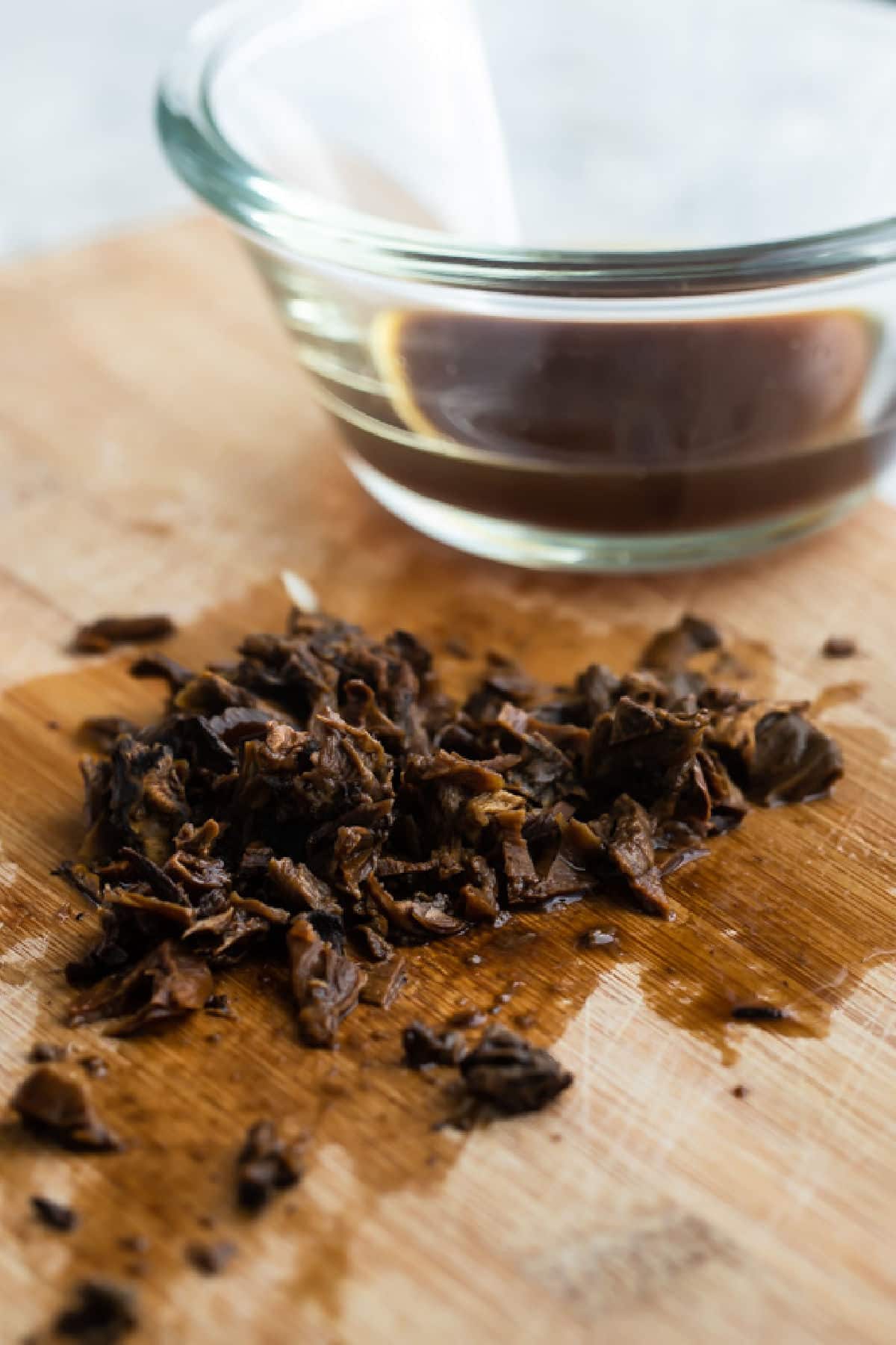 Dried mushrooms that have been rehydrated, minced on a cutting board.