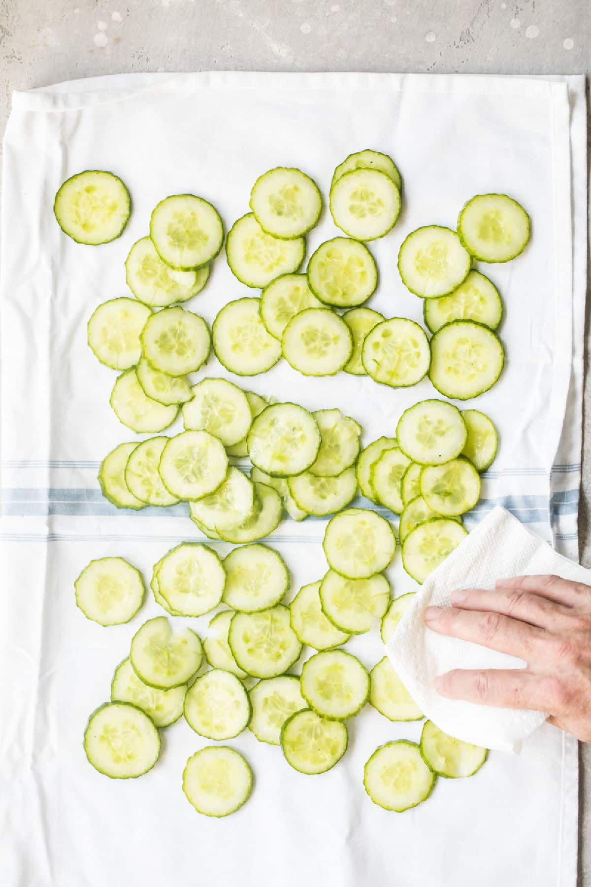 Cucumber slices being patted dry with a towel.