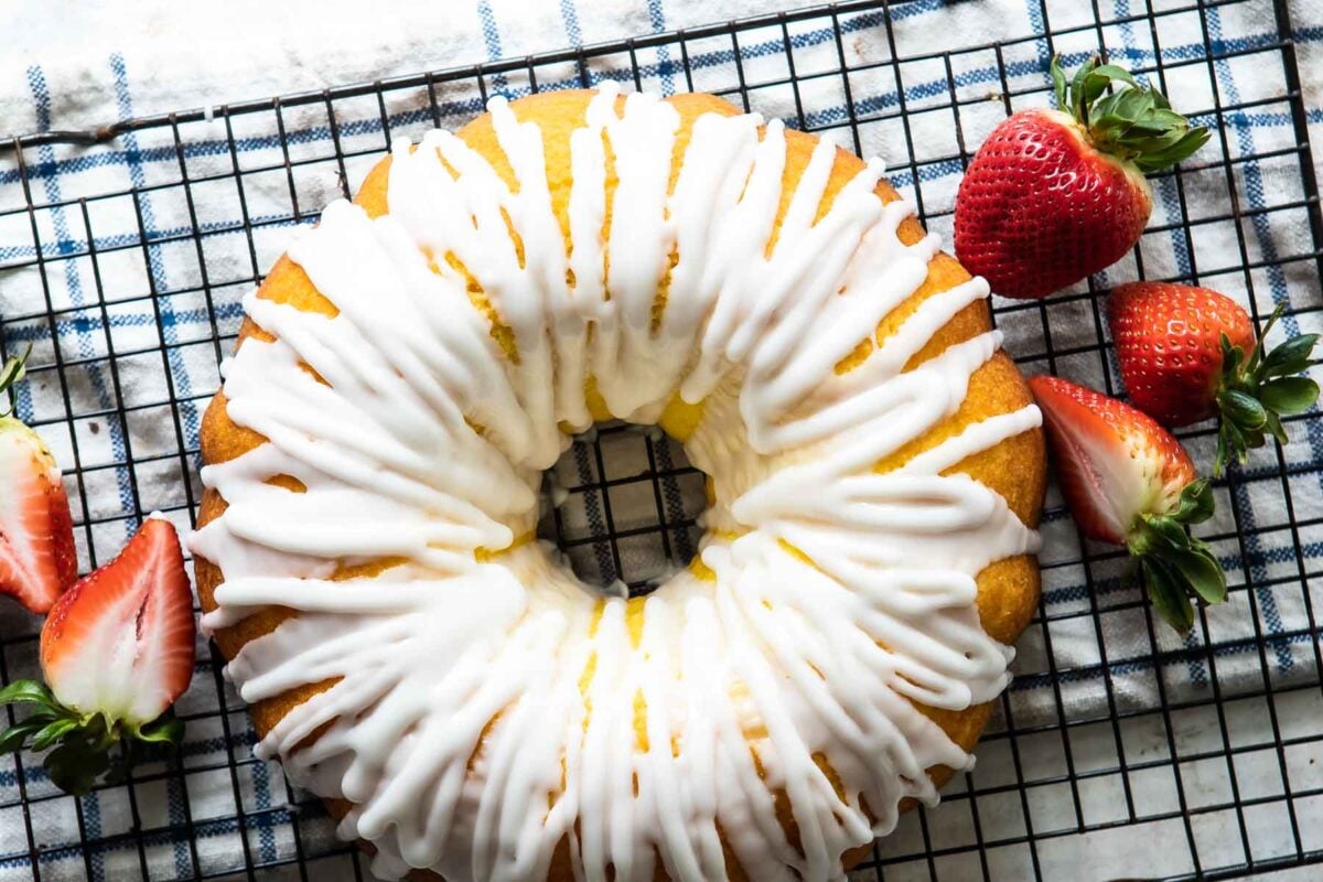 An unsliced lemon bundt cake with lots of glaze and some strawberries nearby.