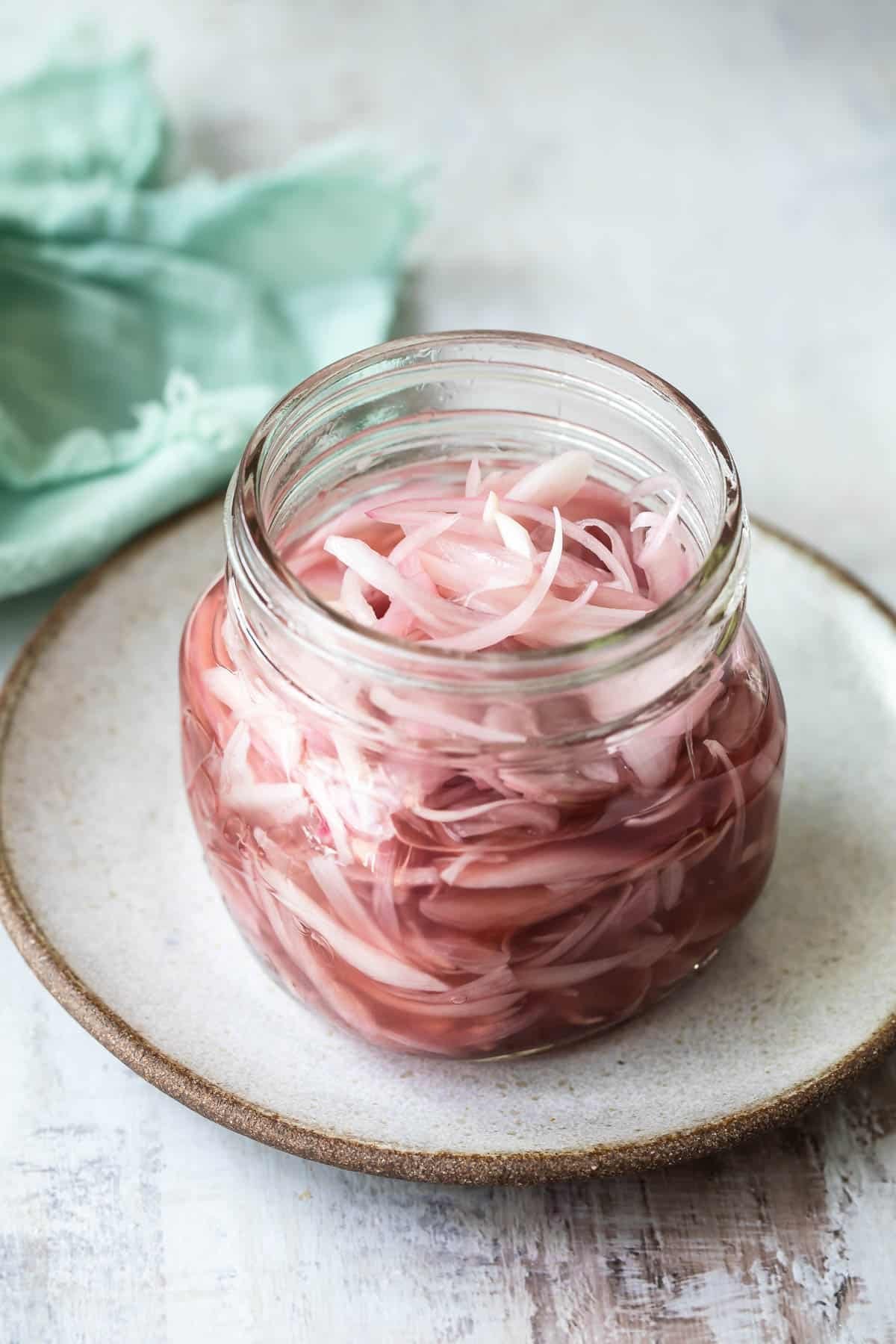 A jar of pickled shallots next to a spoon.