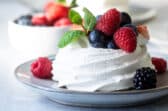 A Schaum torte covered in berries on a gray plate.