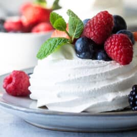 A Schaum torte covered in berries on a gray plate.
