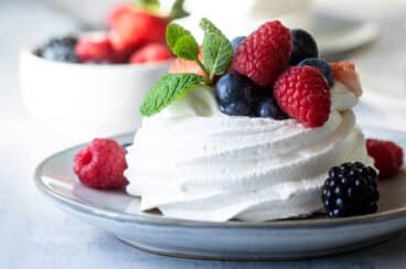A Schaum torte covered in berries on a gray plate.