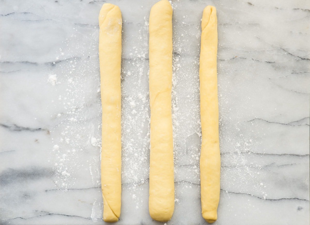 An overhead shot of three long thin rolls of challah bread dough.