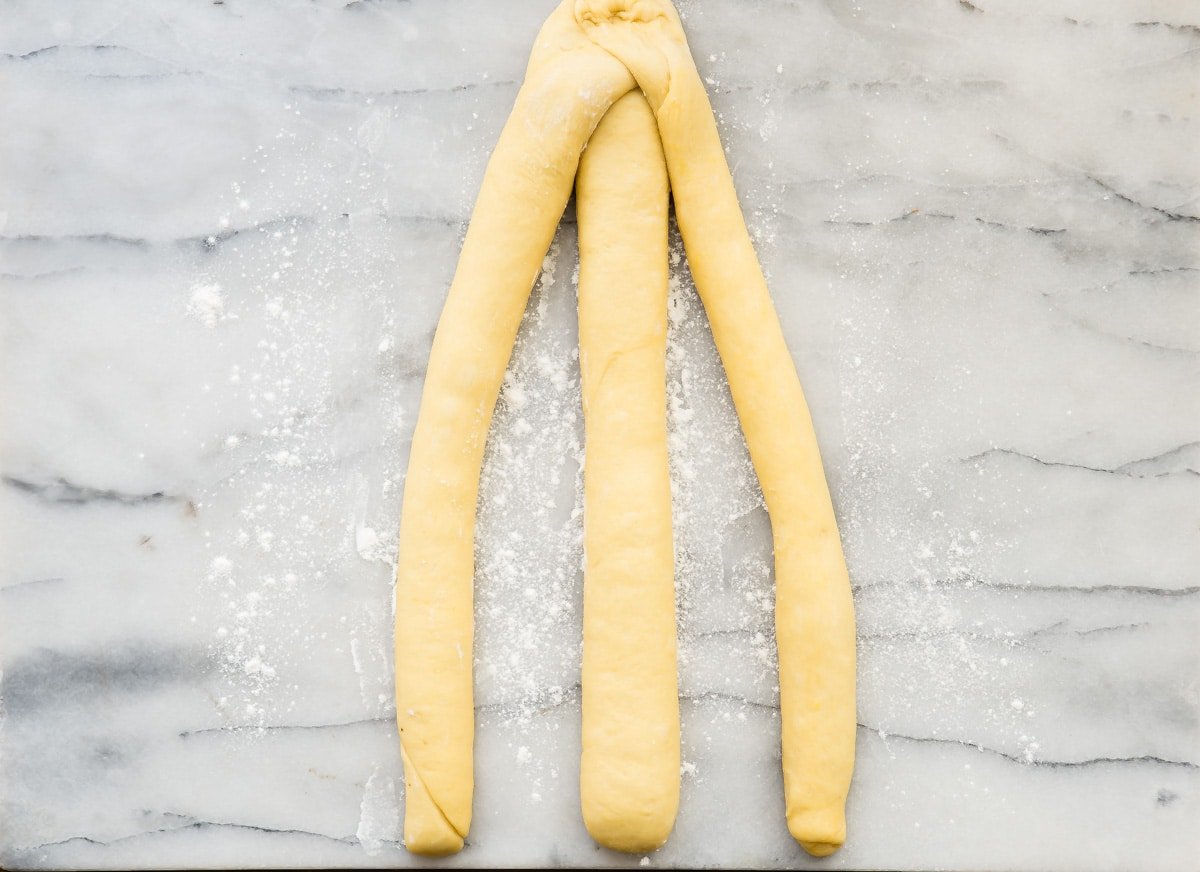 An overhead shot of three long thin rolls of challah bread dough.