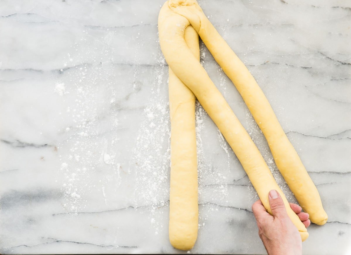 An overhead shot of three long thin rolls of challah bread dough.