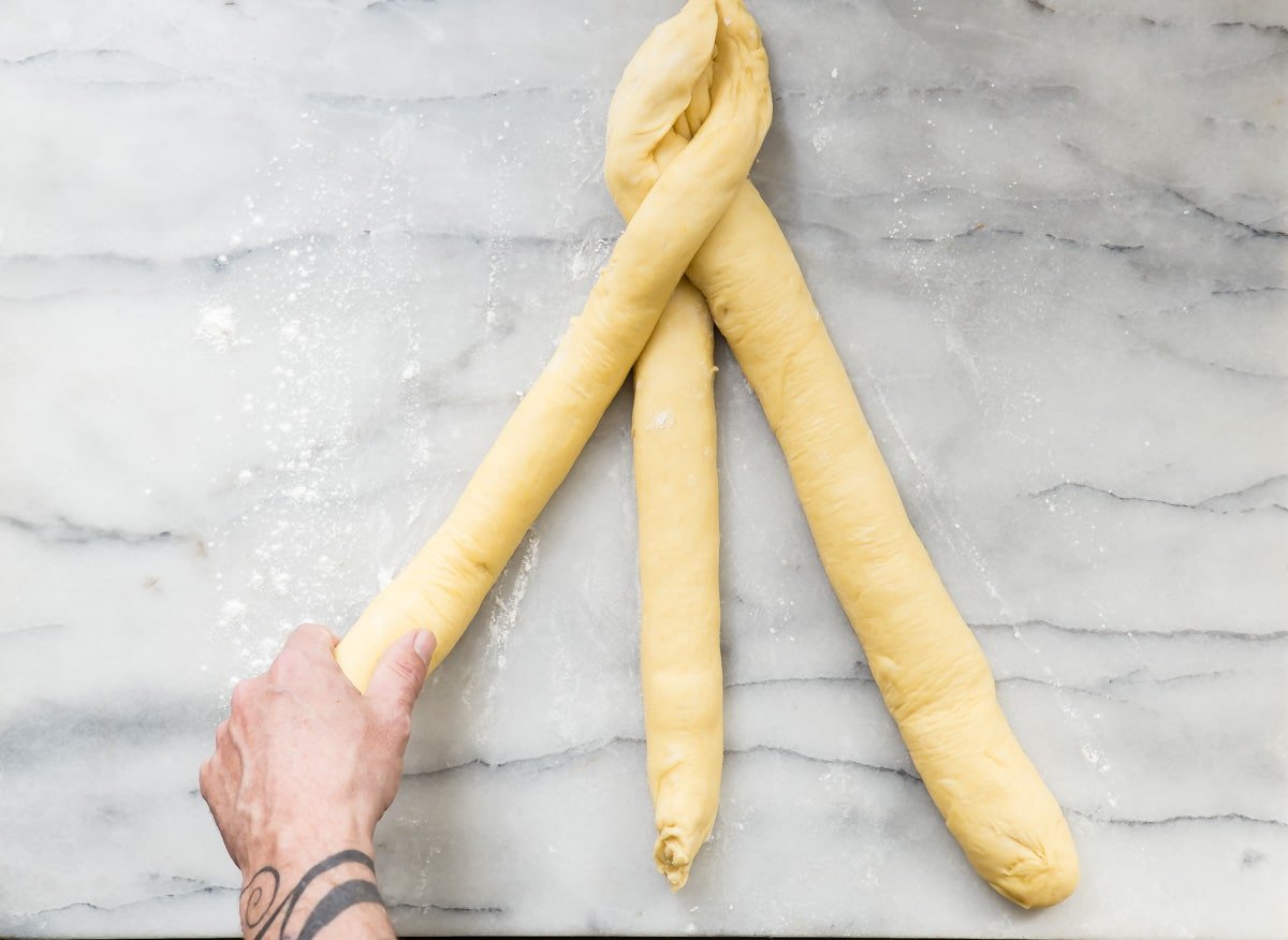 An overhead shot of three long thin rolls of challah bread dough.
