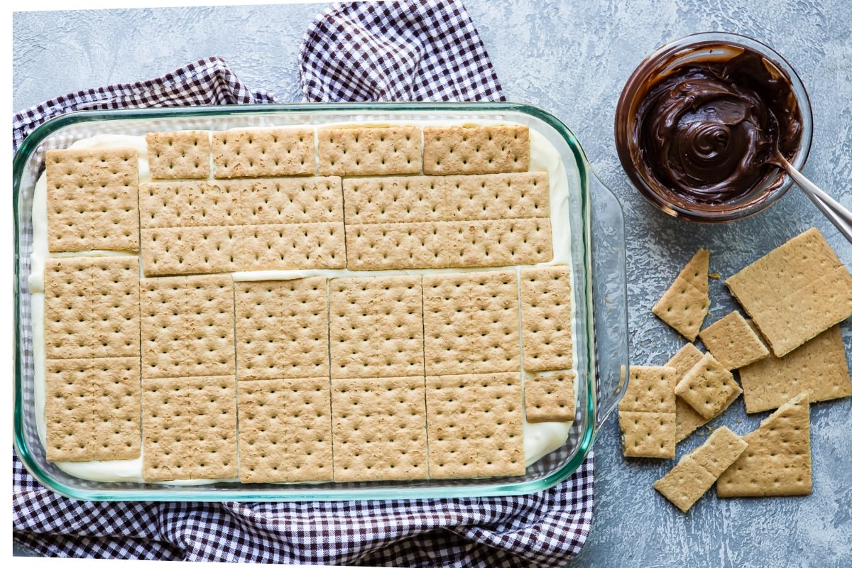 Layering graham crackers on top of vanilla pudding for eclair cake.