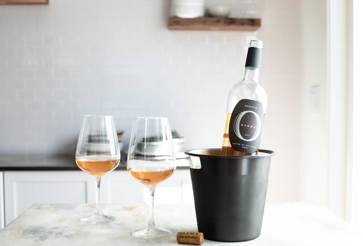 Two glasses of rose wine next to an open bottle in a bottle chiller.