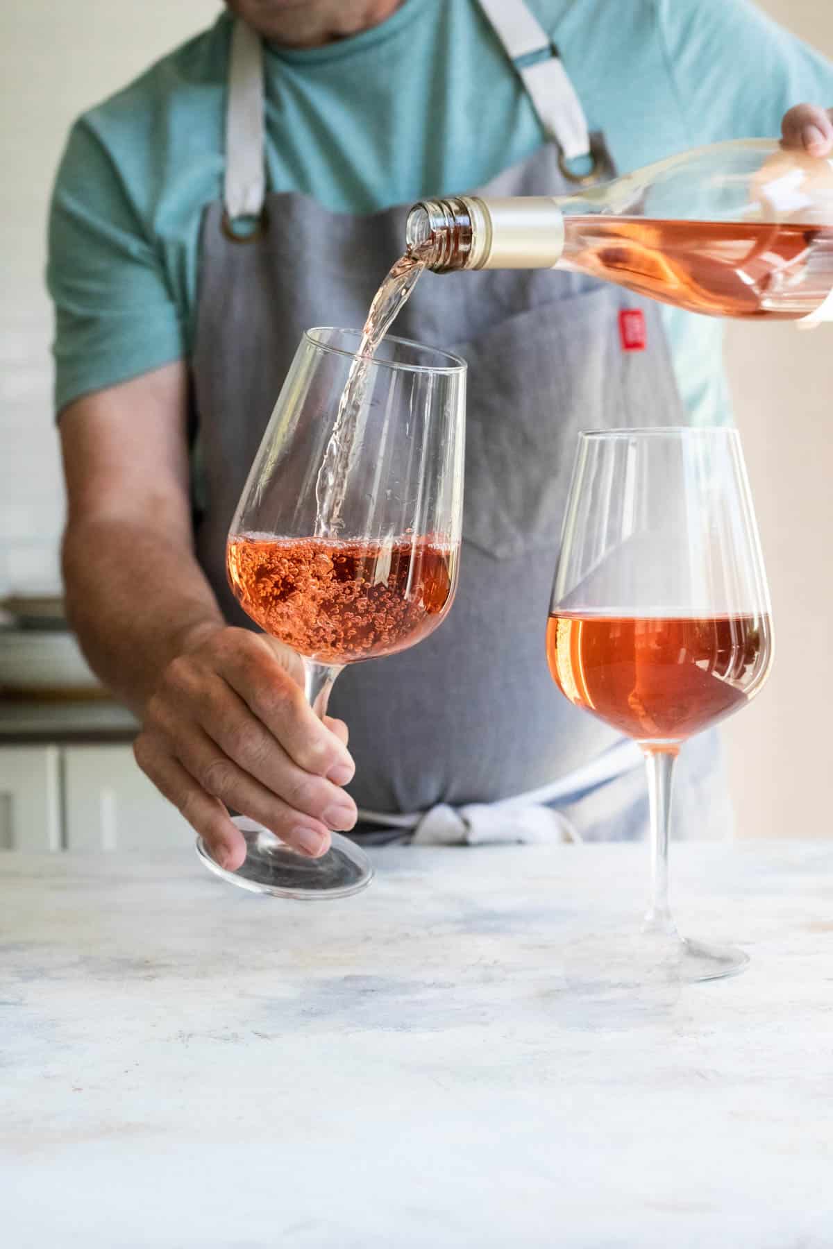 Somebody pouring two glasses of rose wine.