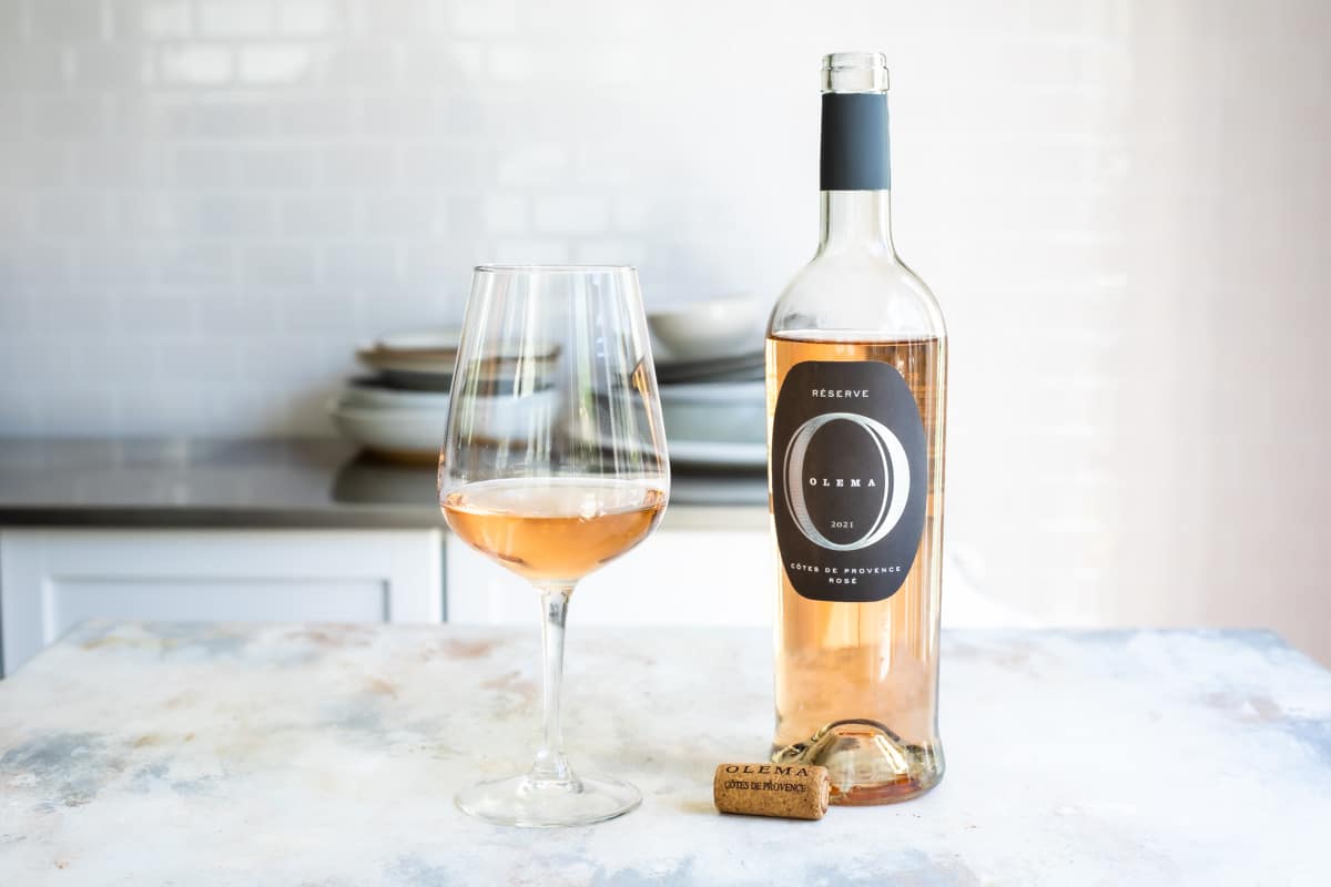A bottle of rose wine next to a glass of the same.