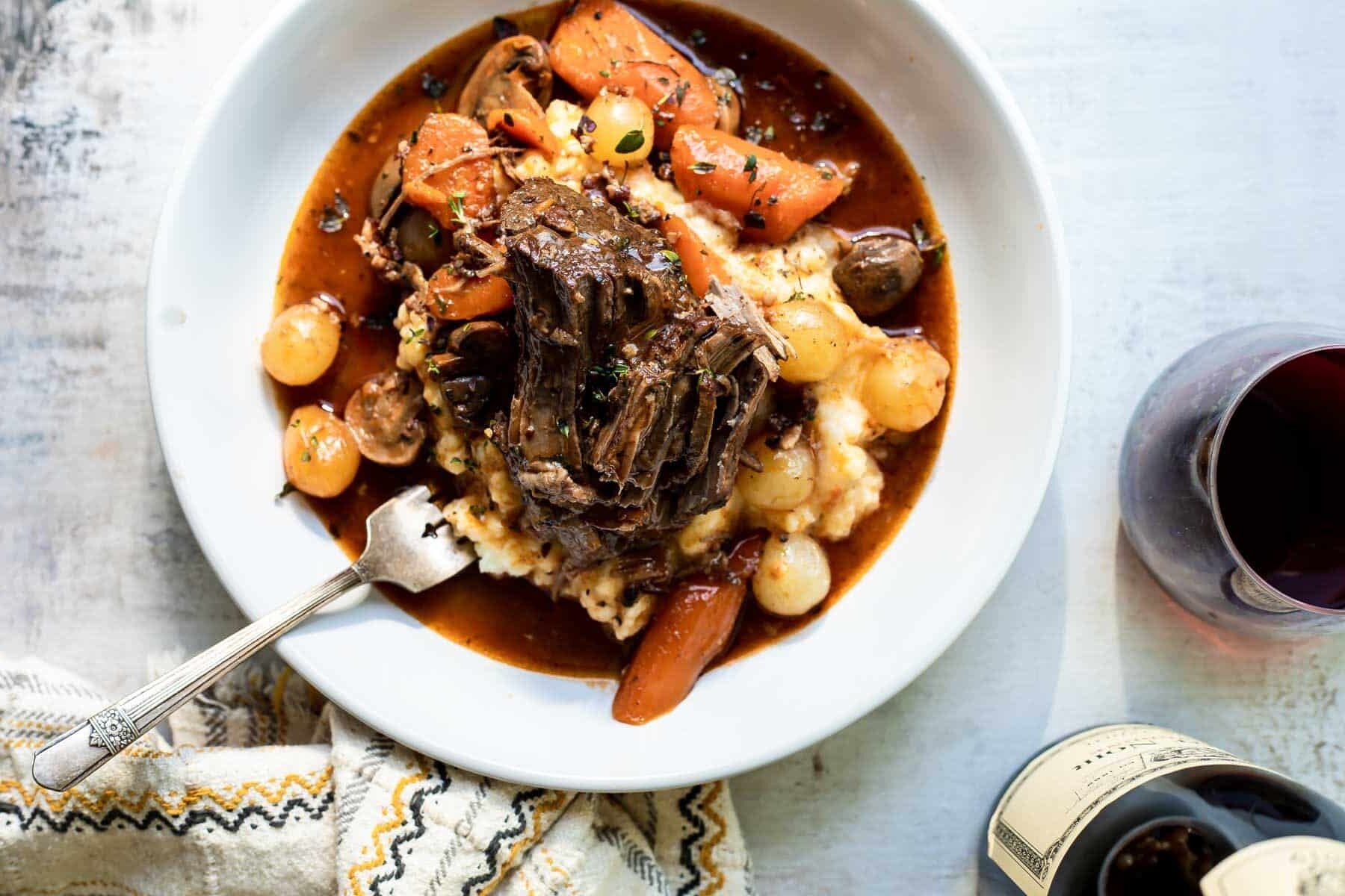 A white bowl of beef bourguignon and mashed potatoes.