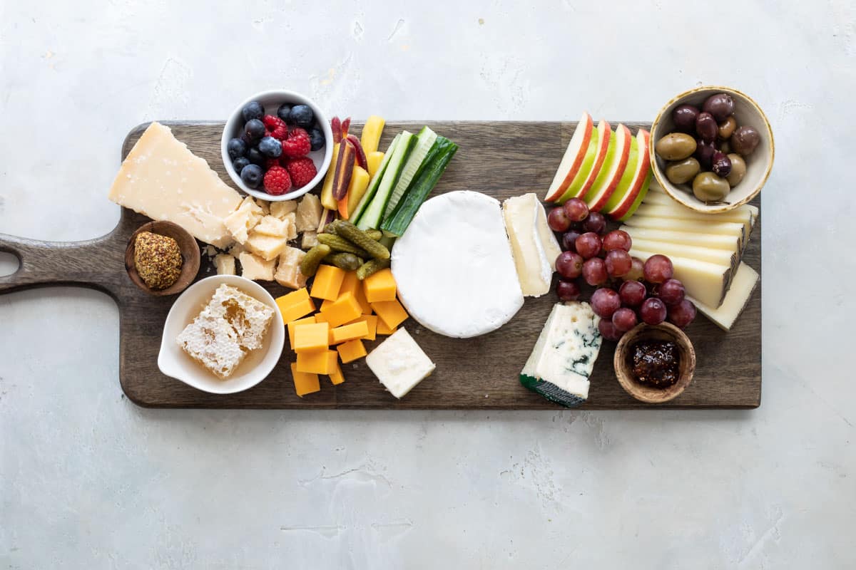 A cheese board filled with fruits, vegetables, nuts, crackers, and cheese.