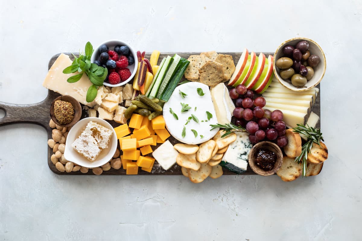 A cheese board filled with fruits, vegetables, nuts, crackers, and cheese.