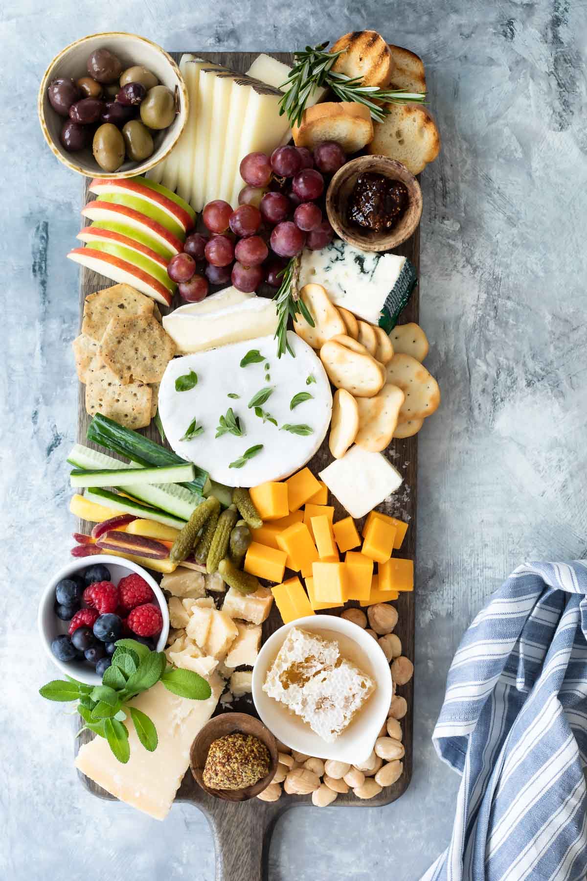 A cheese board filled with fruits, vegetables, nuts, crackers, and cheese.