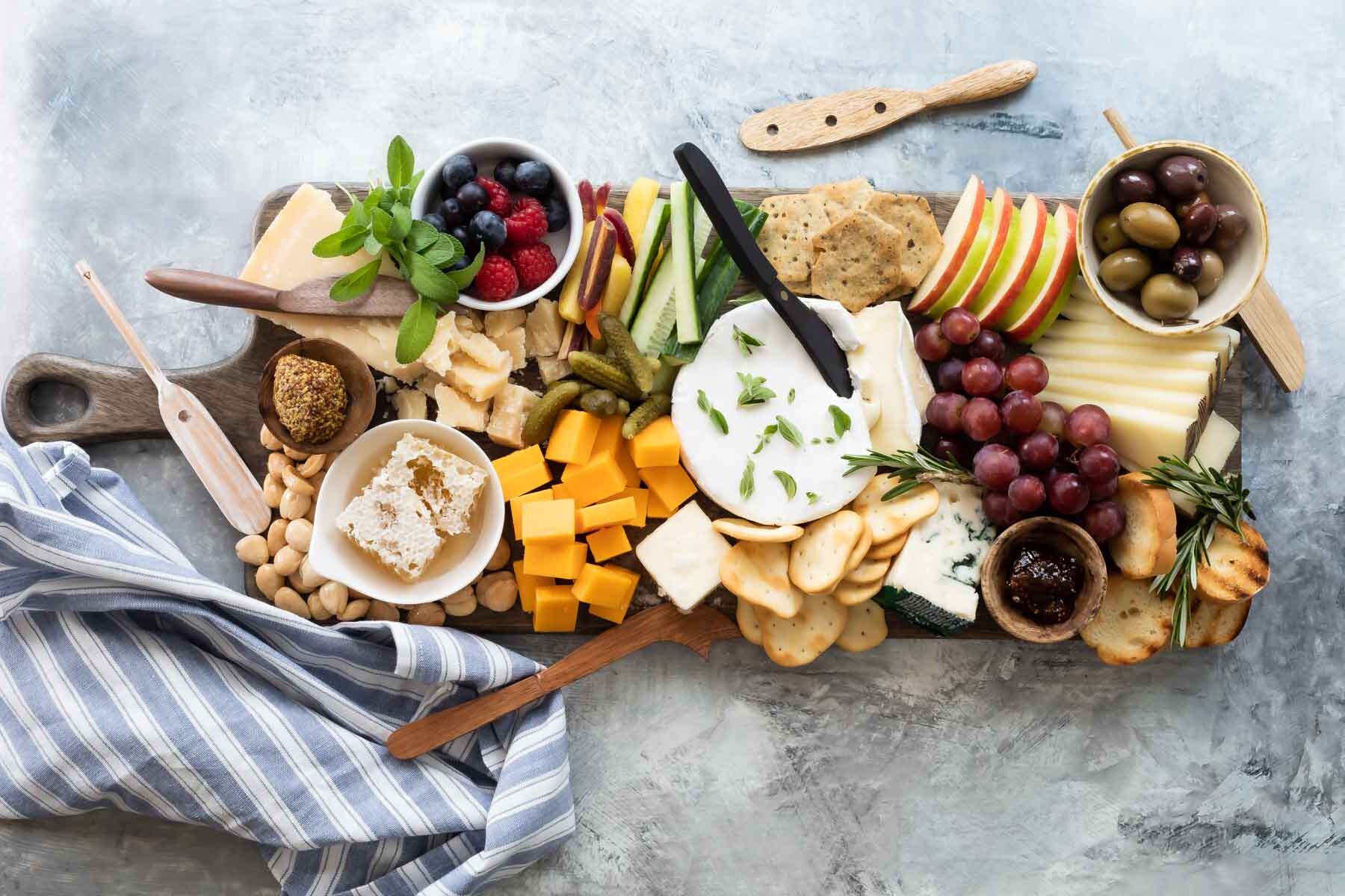 A cheese board filled with fruits, vegetables, nuts, crackers, and cheese.
