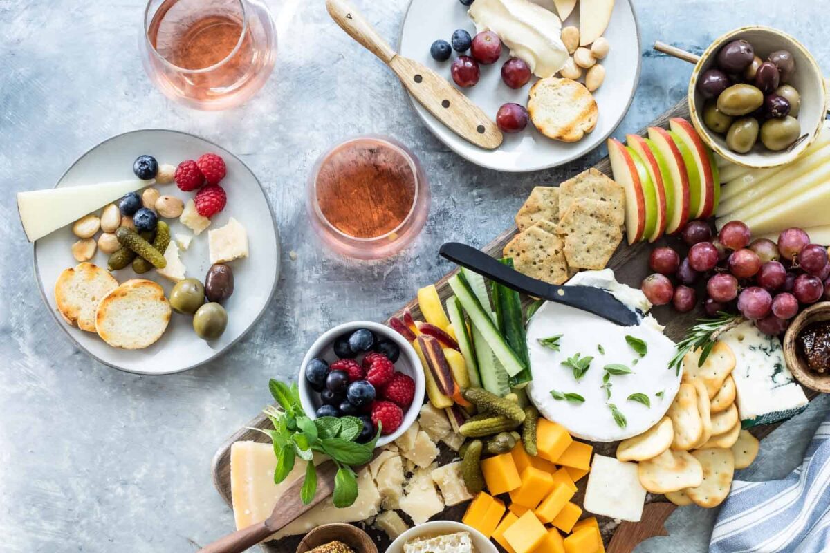 A cheese board filled with fruits, vegetables, nuts, crackers, and cheese.