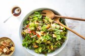 Fattoush in a white bowl with wooden serving utensils.