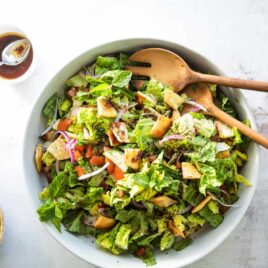 Fattoush in a white bowl with wooden serving utensils.